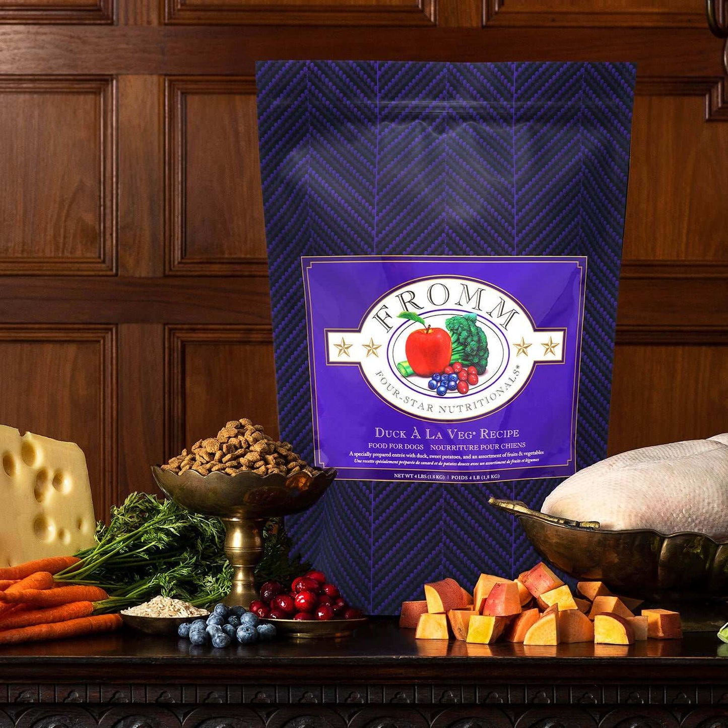 Fromm Four-Star Duck A La Veg dog food bag with fresh vegetables, fruits, and raw duck displayed on table