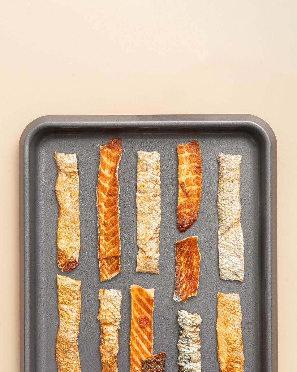 Assorted strips of smoked salmon skin jerky on a gray tray, natural high-protein dog treat rich in omegas.