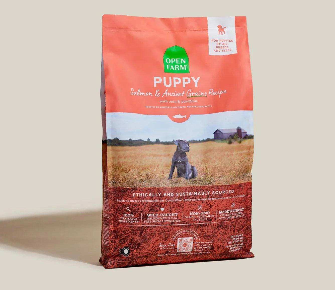 Open Farm Puppy Salmon & Ancient Grain Recipe kibble bag with farm field background and dog image, protein-packed puppy food with wild-caught salmon and ancient grains.