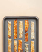 Assorted strips of smoked salmon skin jerky on a gray tray, natural high-protein dog treat rich in omegas.