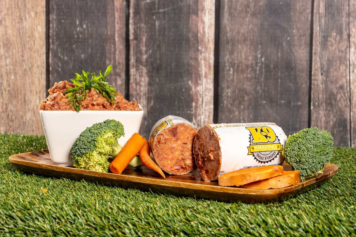 K-9 Kraving Chicken & Vegetable Raw Dog Food with broccoli, carrots, and sweet potatoes on a wooden tray.