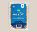 Dog food in a clear sealed pouch with a blue Surf & Turf Grain-Free label and visible mixed ingredients around the edges.